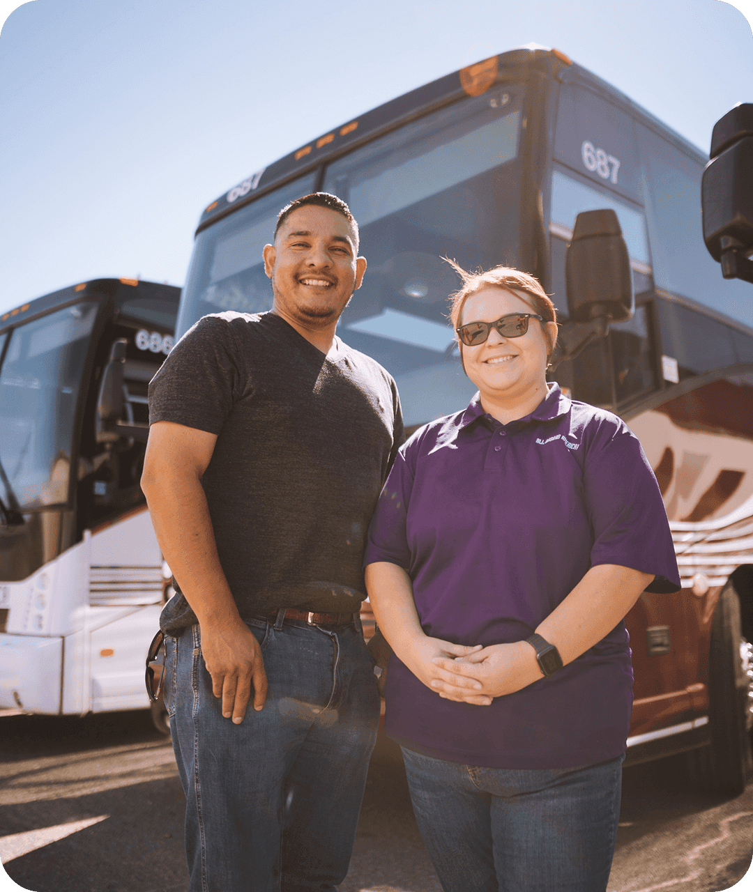 Two smiling employees stand together in front of an All Aboard America bus.