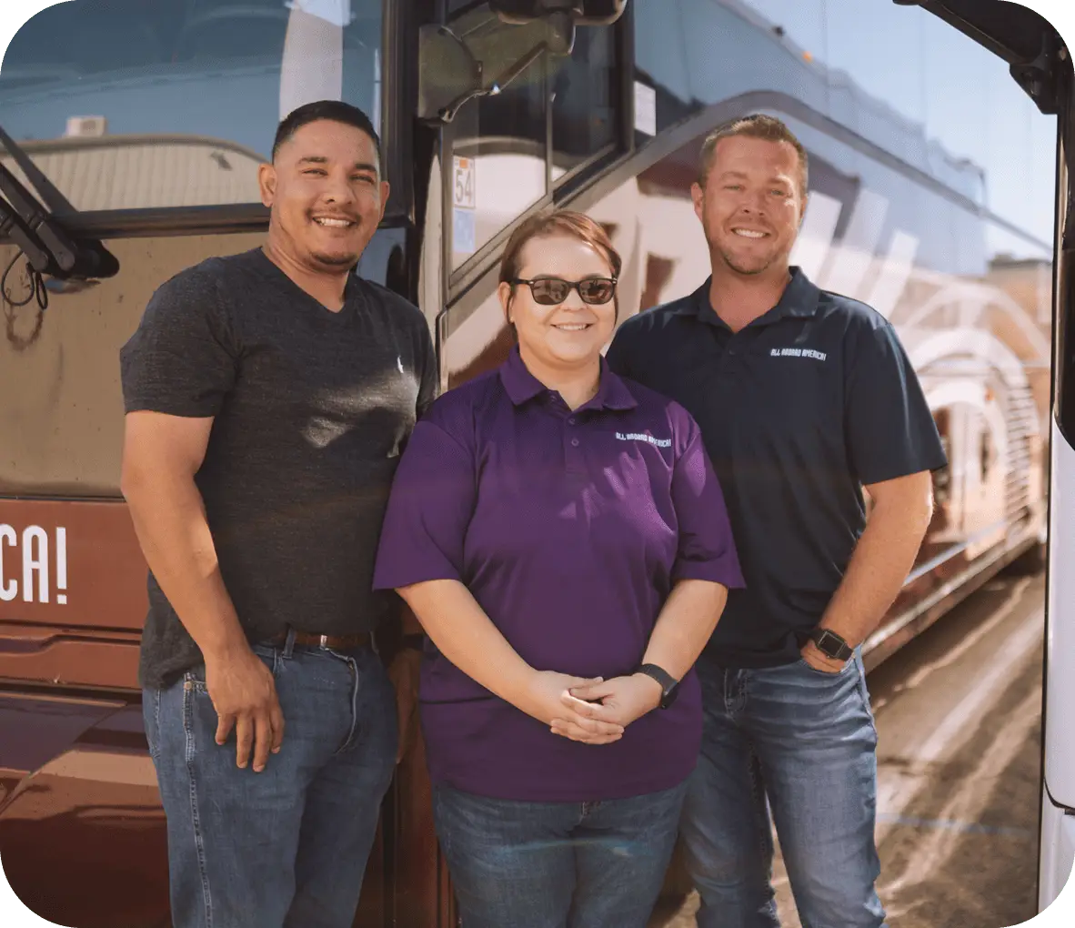Three smiling employees stand together in front of an All Aboard America bus.