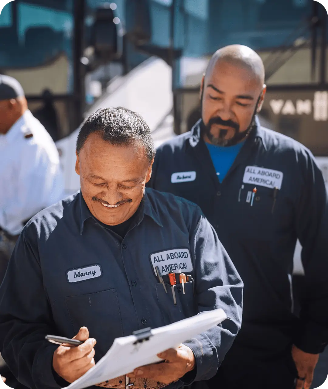 Two All Aboard America mechanics in uniform review a clipboard together at the bus fleet depot