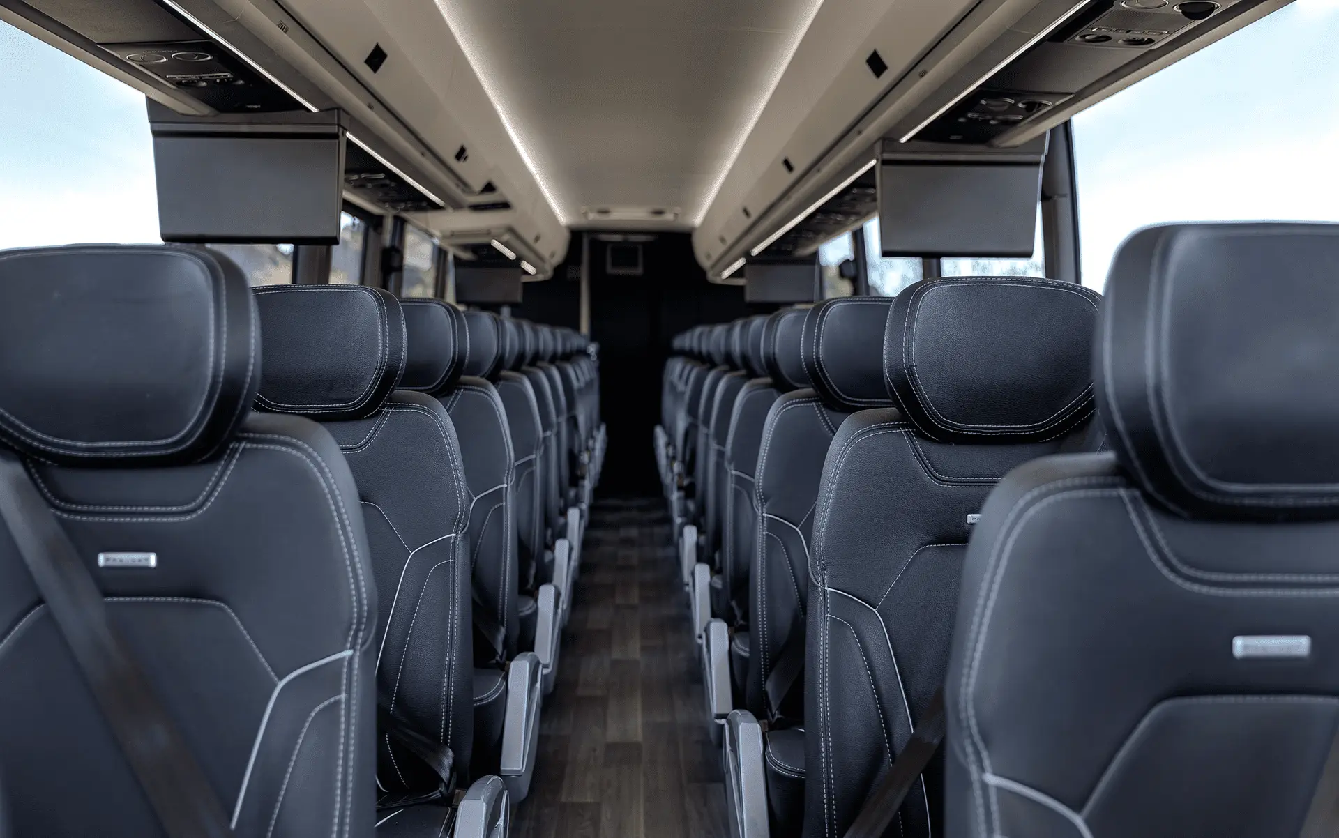 The inside of a bus is shown with empty seats. Some features shown include seat belts, media screens, and interior lighting.