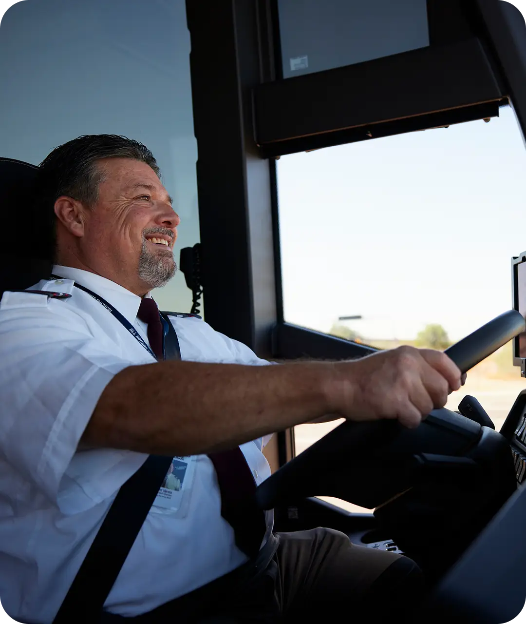 A smiling bus driver for All Aboard America sits in the bus's driver's seat with her hands on the steering wheel.