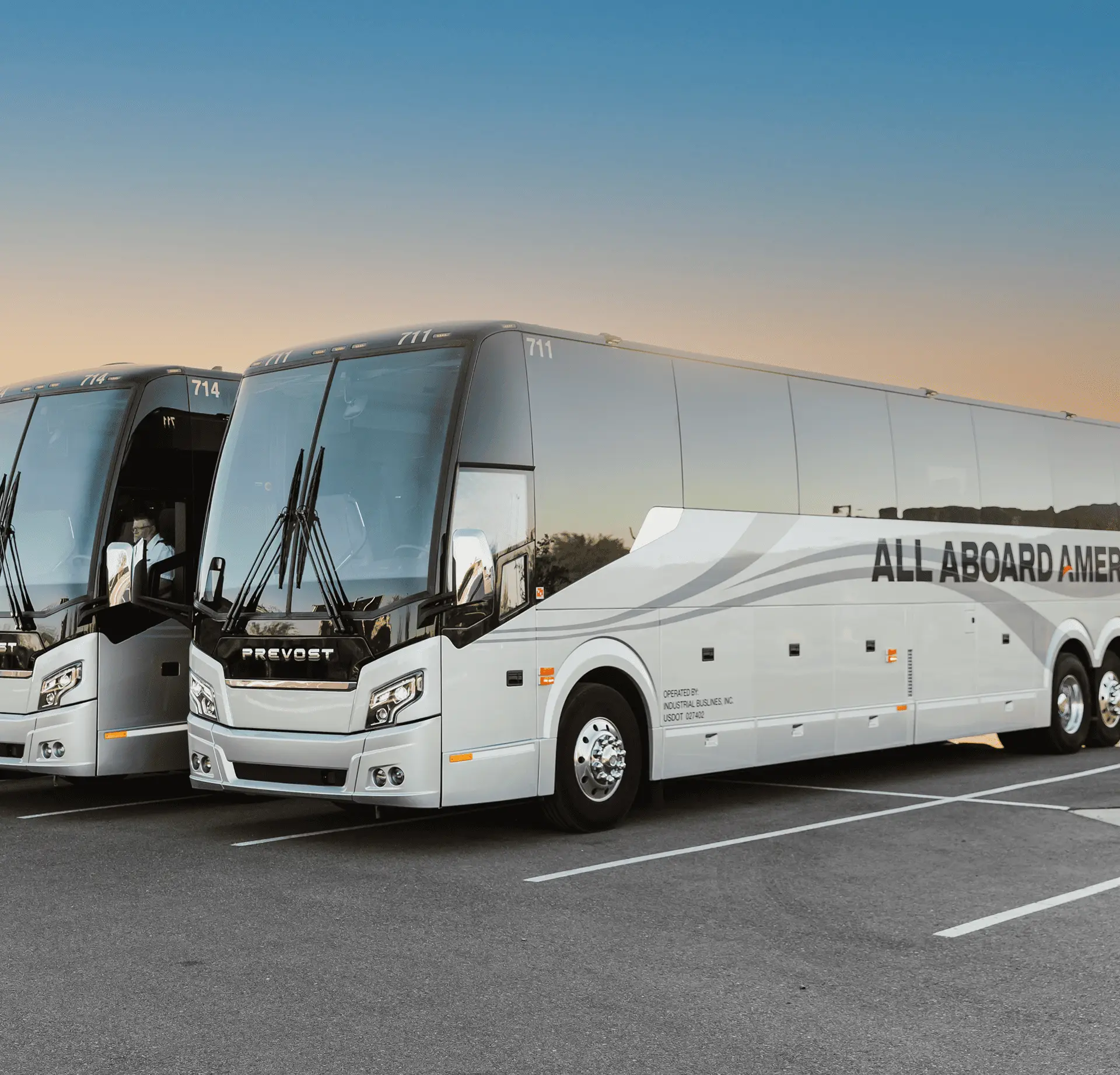Two All Aboard America Prevost motorcoaches parked side by side in a lot at dusk