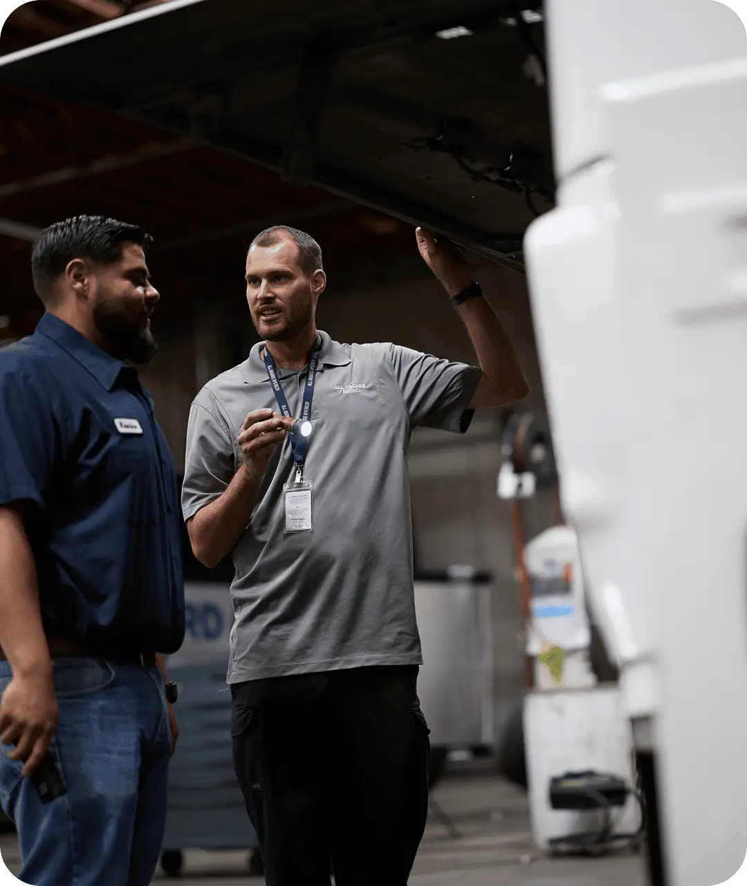 Two All Aboard America mechanics inspect a bus engine compartment together in the maintenance shop