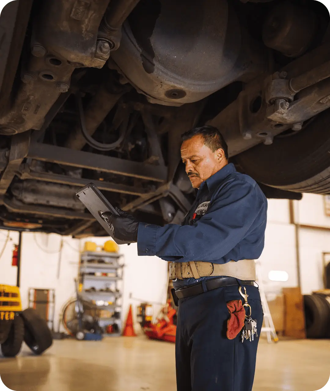 An All Aboard America mechanic uses a tablet to run diagnostics beneath a raised bus in the repair shop