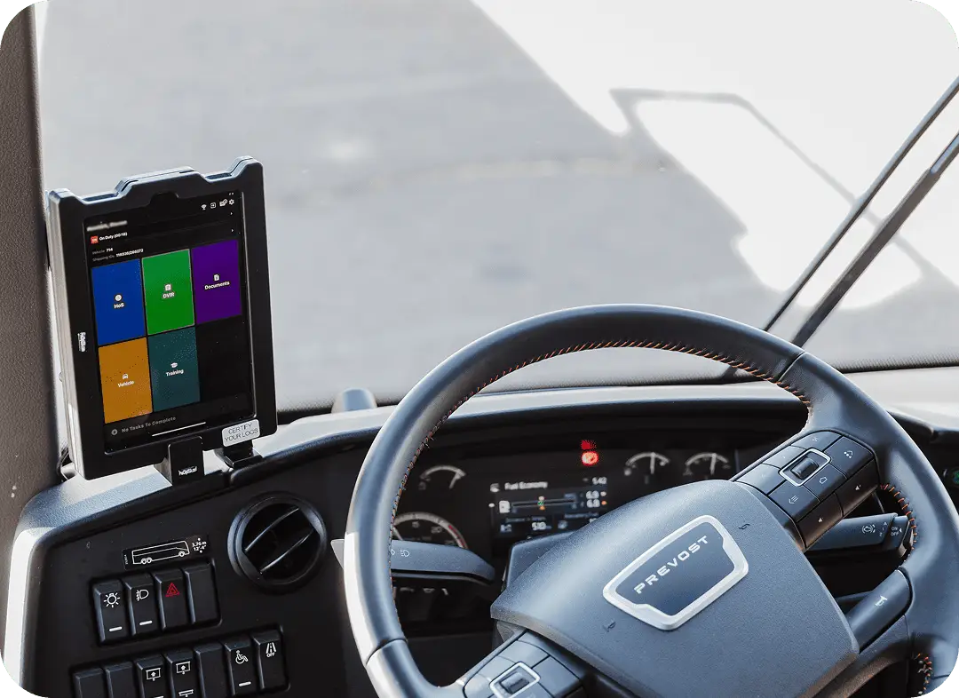 A fleet management tablet mounted on the dashboard of a Prevost motorcoach displaying driver compliance tools