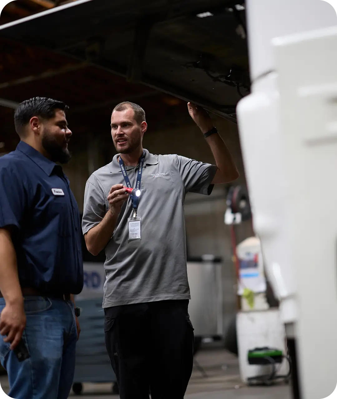 2 All Aboard America employees are reviewing a bus's engine as part of a maintenance check
