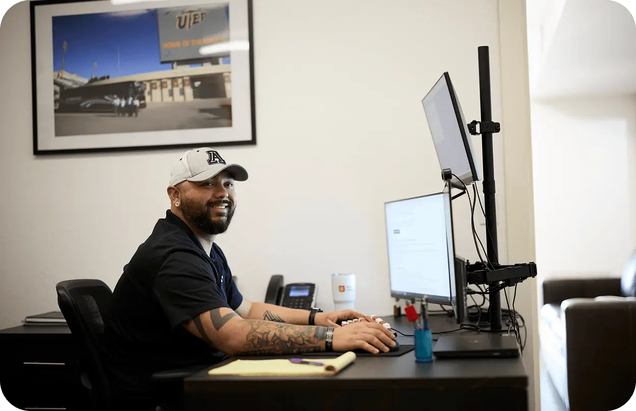 A smiling All Aboard America staff member works at his desk with dual monitors in the office
