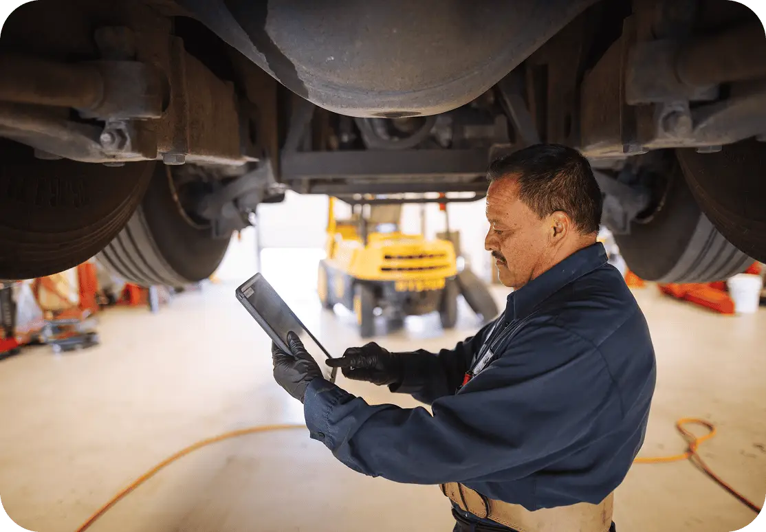 An All Aboard America mechanic uses a tablet to run diagnostics beneath a raised bus in the maintenance shop