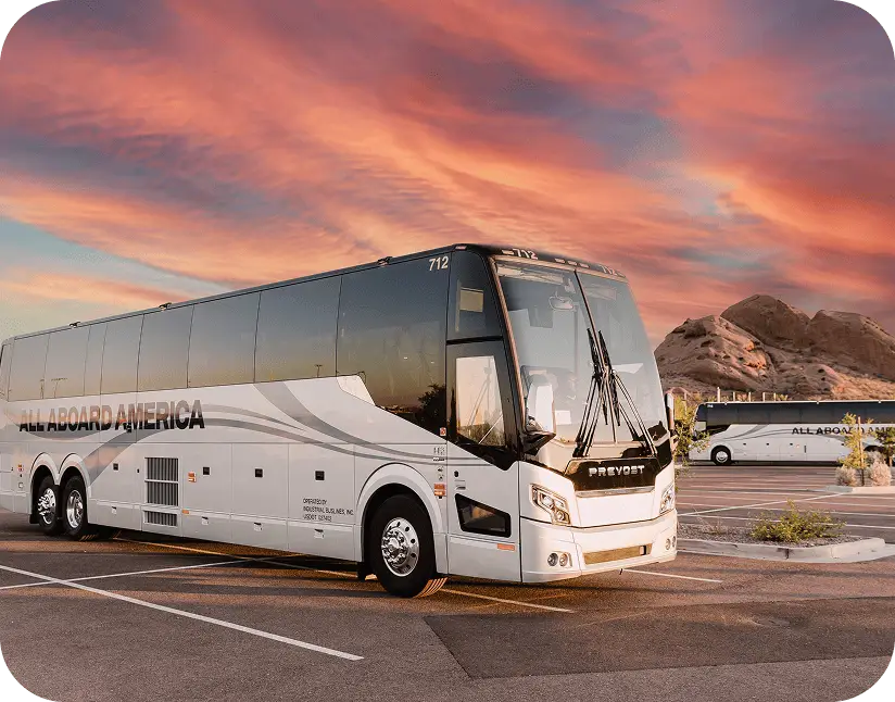 An All Aboard America Prevost motorcoach number 712 parked at sunset with rock formations and another coach in the background