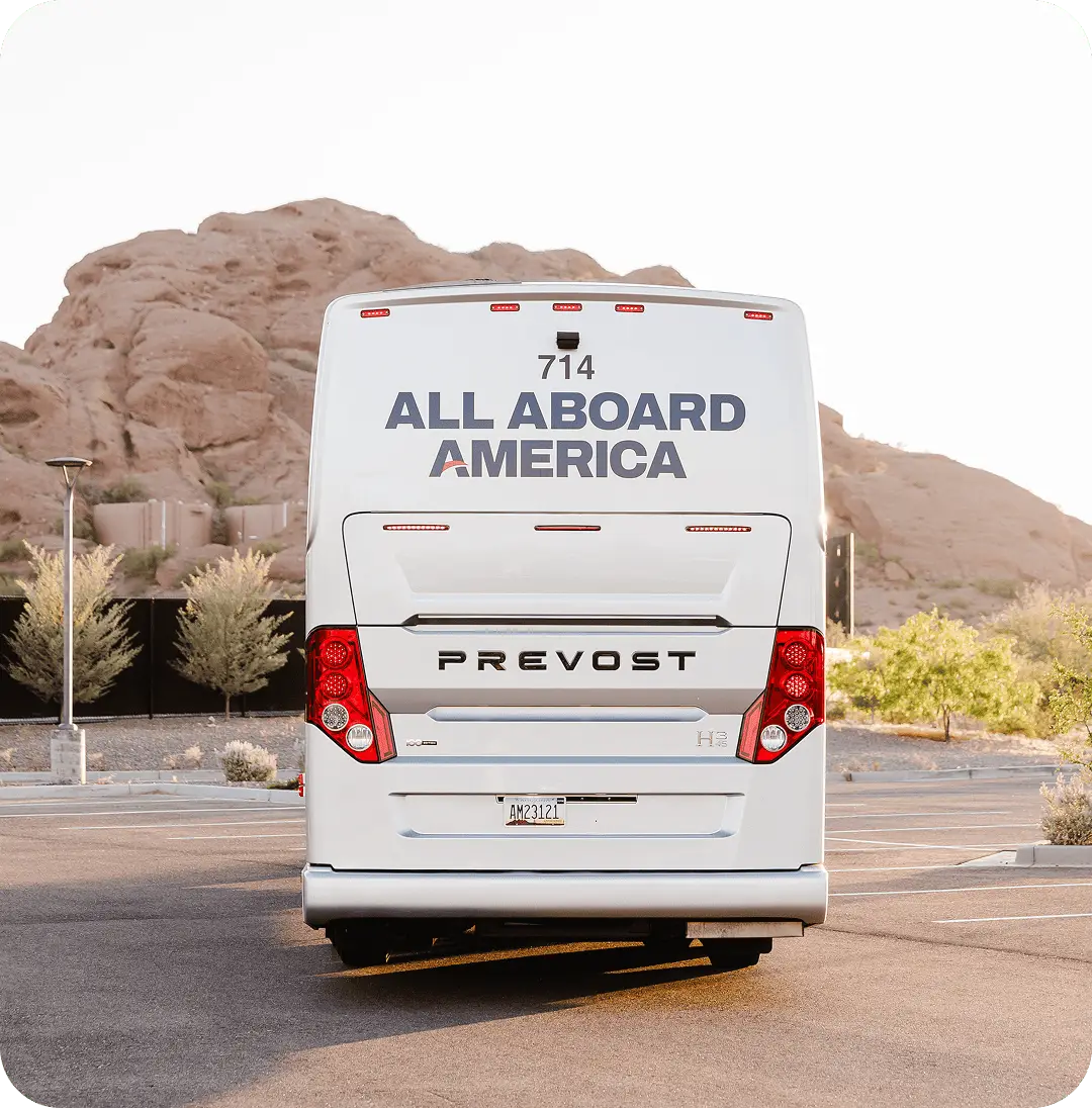Rear view of an All Aboard America Prevost motorcoach number 714 parked in a desert lot with red rock formations