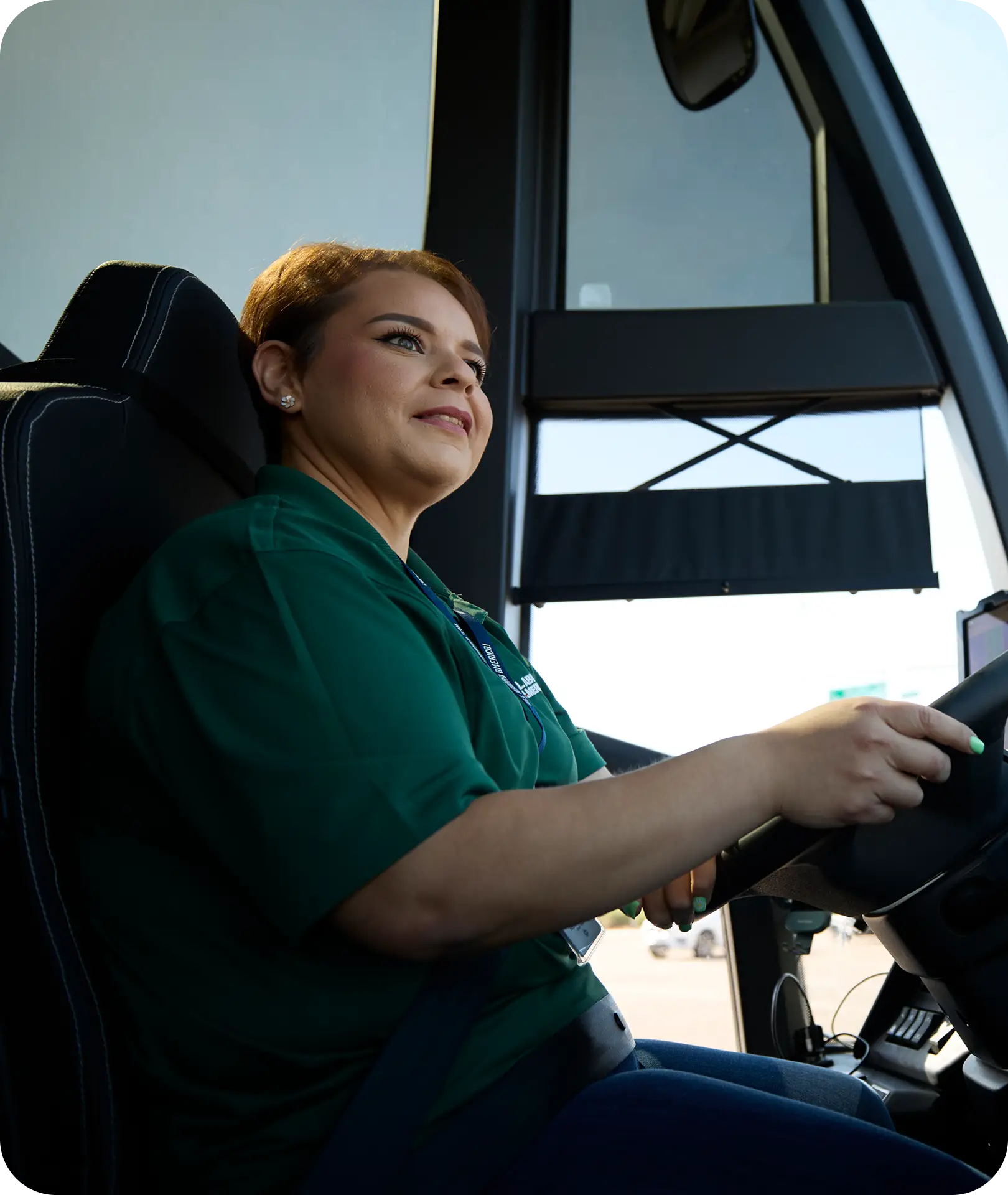 A smiling All Aboard America female driver in a green polo sits behind the wheel of a motorcoach