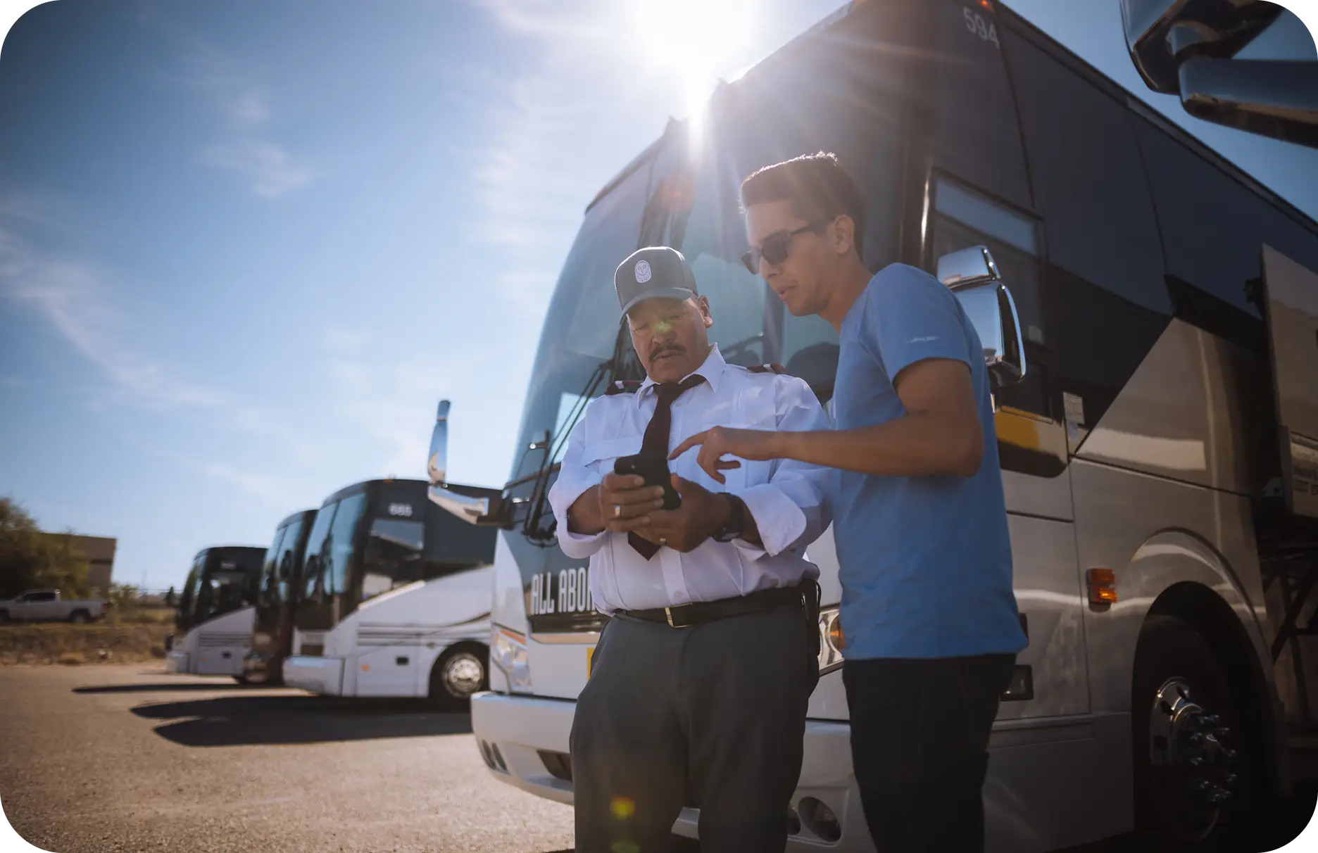 An All Aboard America driver and customer review trip details on a phone in front of a fleet of buses in Midland Texas
