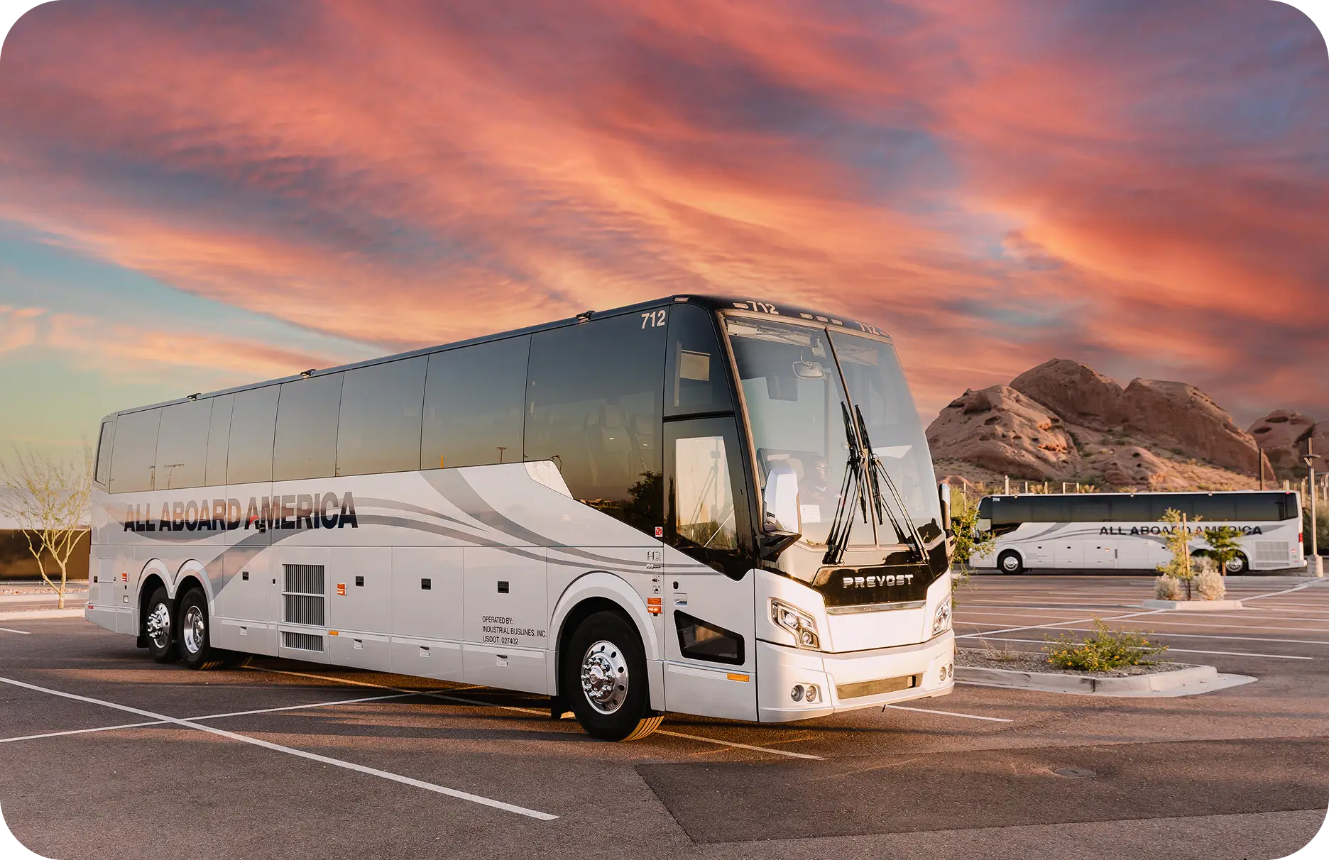 An All Aboard America Prevost motorcoach parked at sunset with desert rock formations near Phoenix Arizona