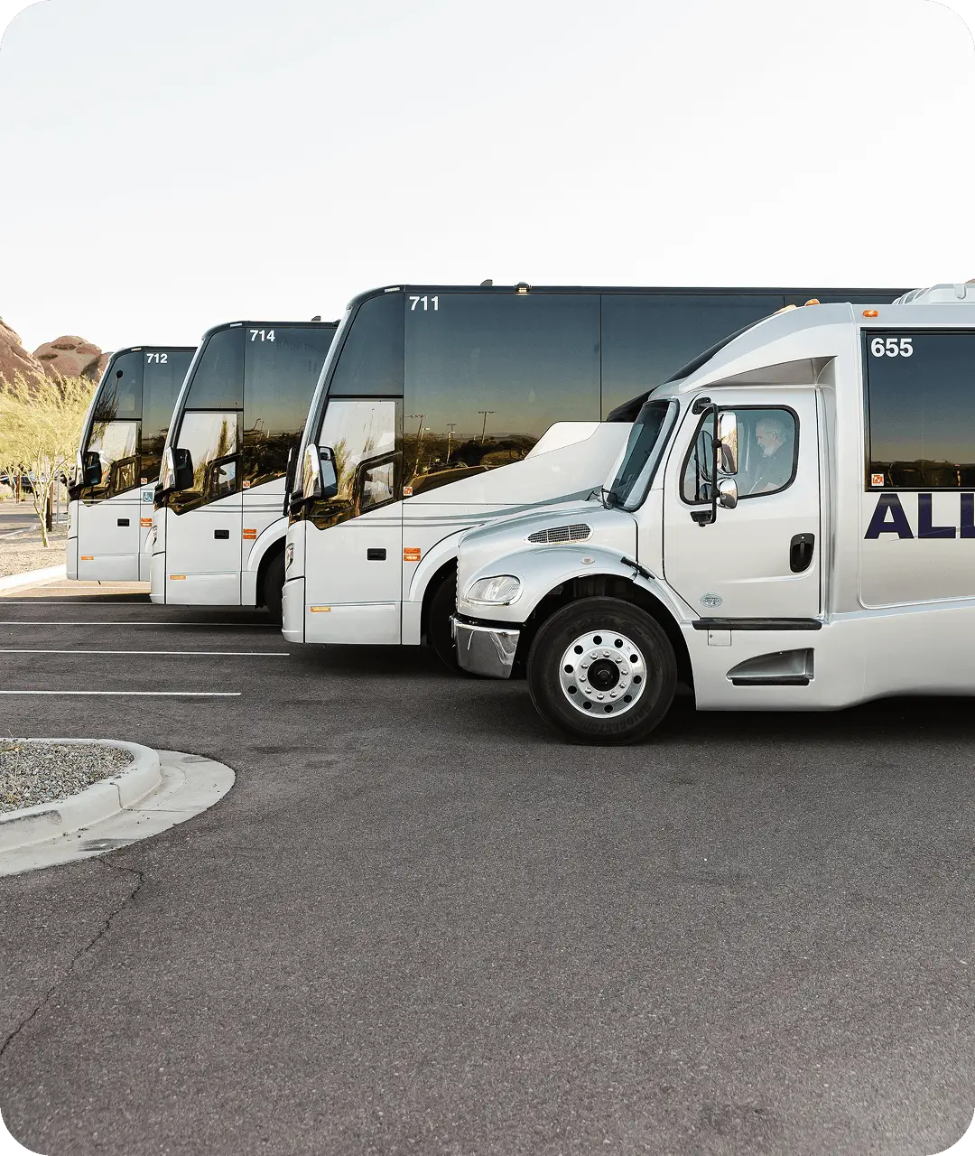 A fleet of All Aboard America motorcoaches and a mini coach lined up in a desert parking lot with rock formations