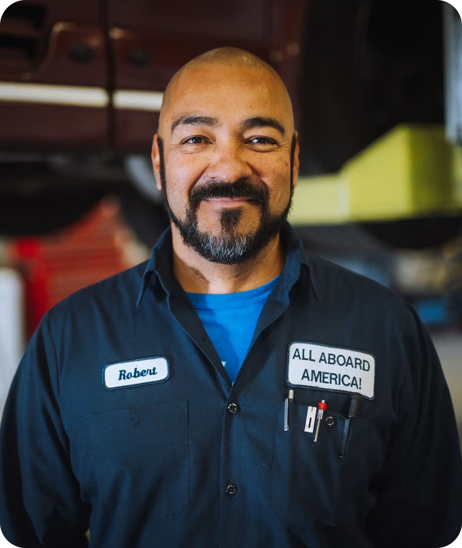 Robert an All Aboard America mechanic smiles in uniform inside the bus repair shop