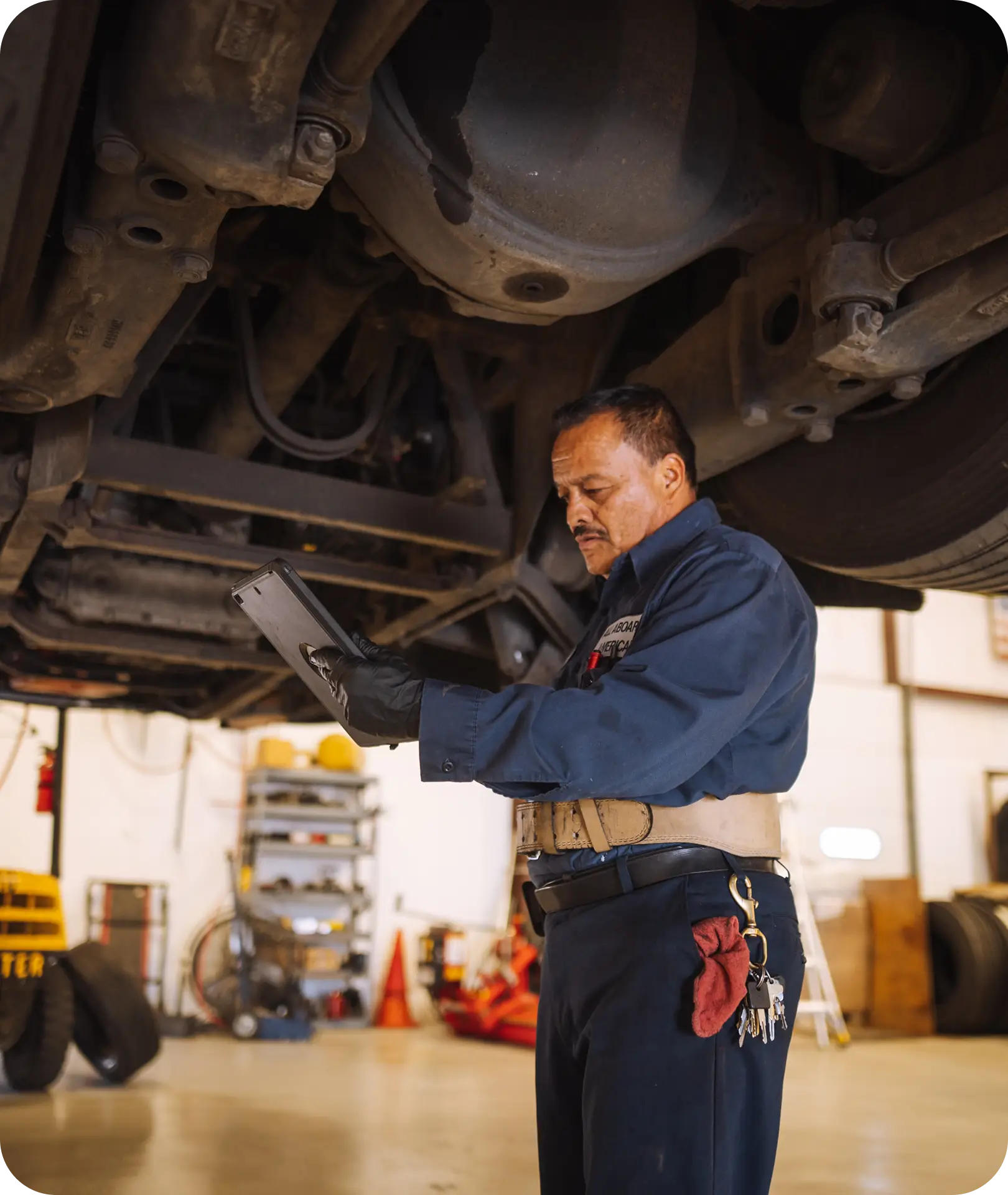 An All Aboard America mechanic uses a tablet to run diagnostics beneath a raised bus in the repair shop