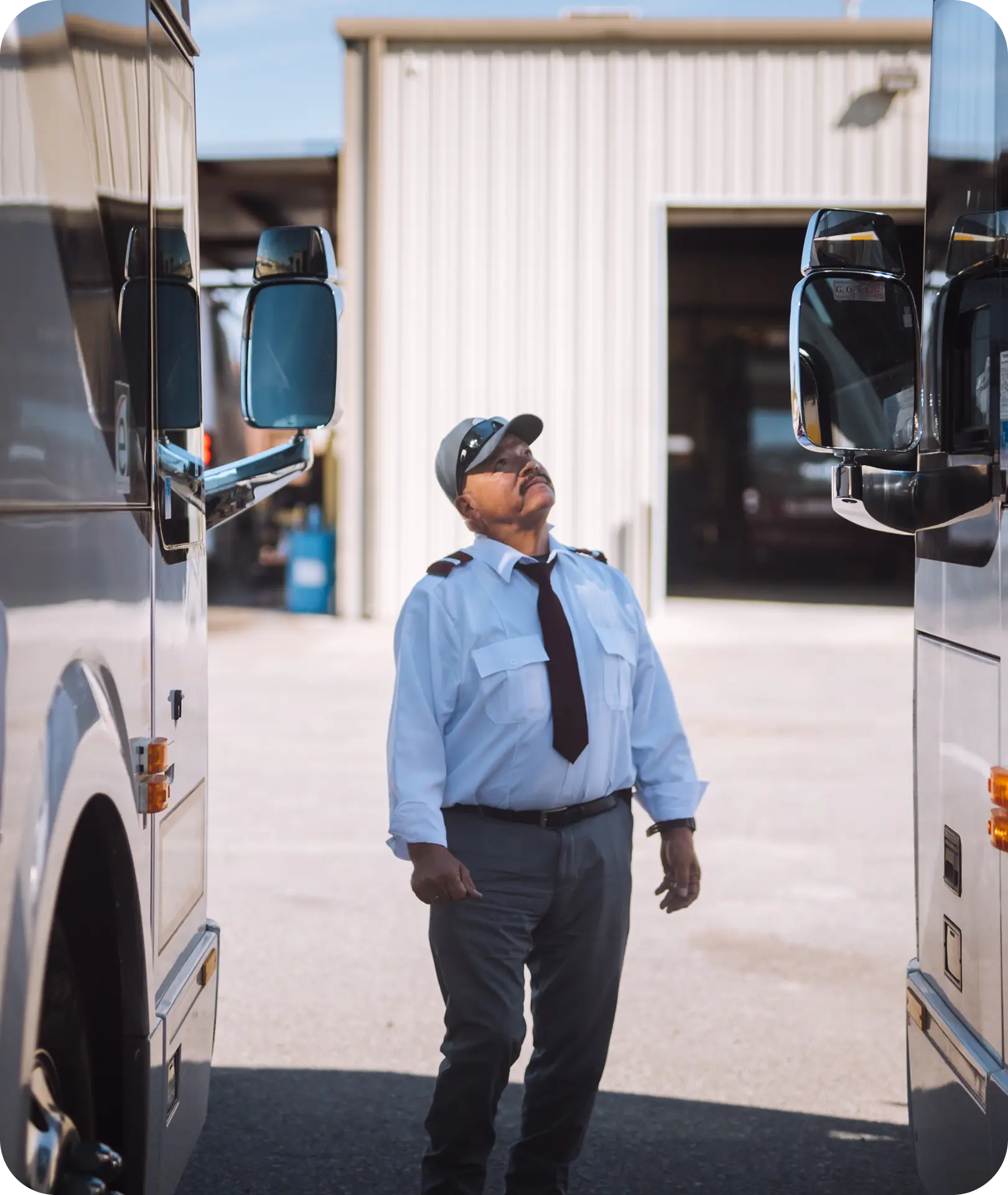 An All Aboard America driver in uniform inspects a bus between two motorcoaches in the depot yard