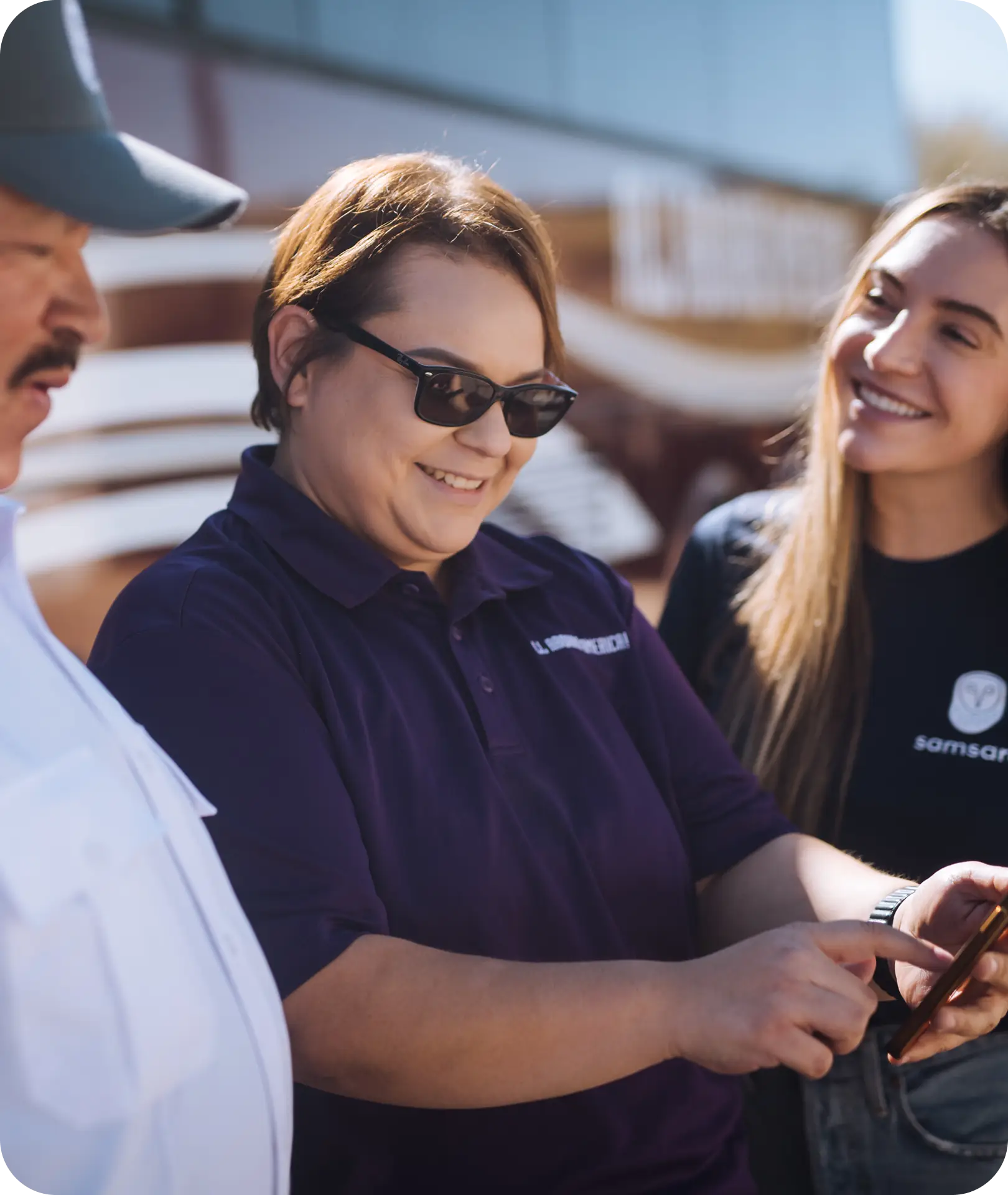 An All Aboard America staff member and a Samsara rep review trip details on a phone with a driver outside
