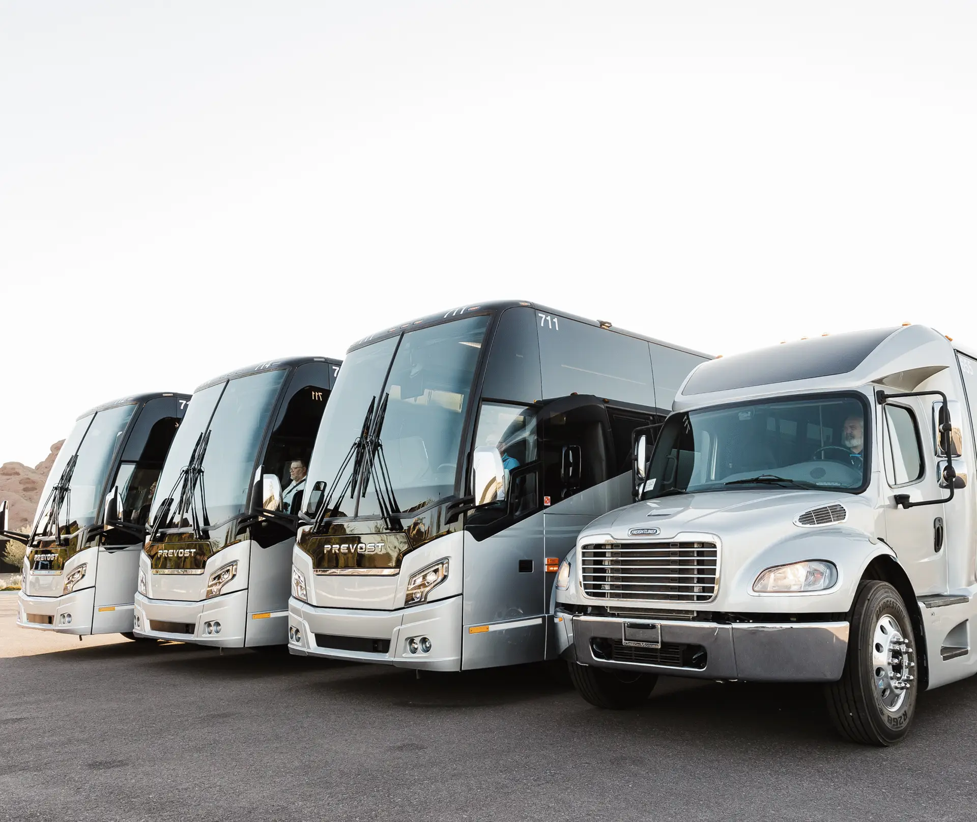 A mixed fleet of All Aboard America Prevost motorcoaches and a smaller bus lined up in a desert parking lot