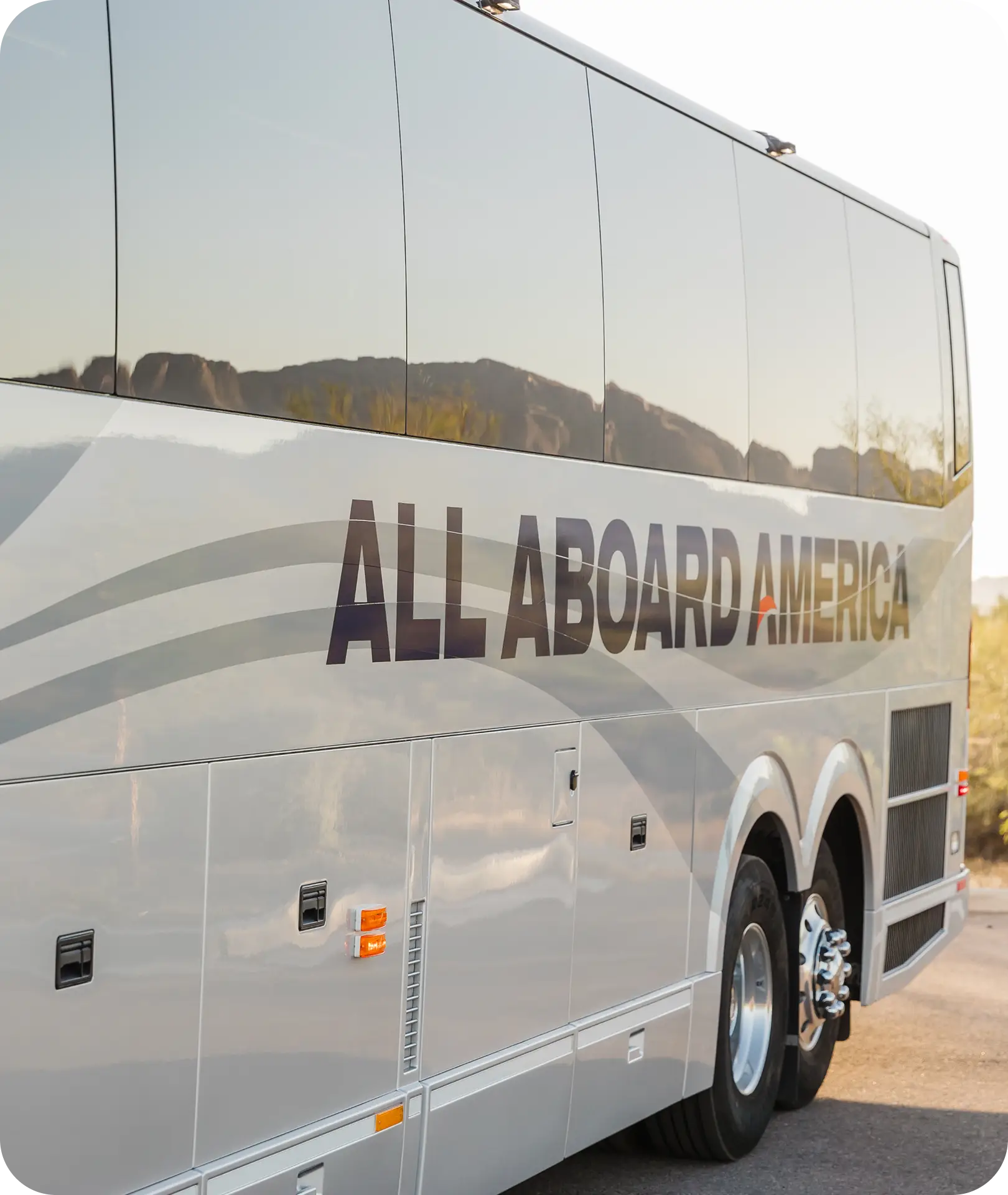Side view of an All Aboard America motorcoach with desert rock formations reflected in the windows