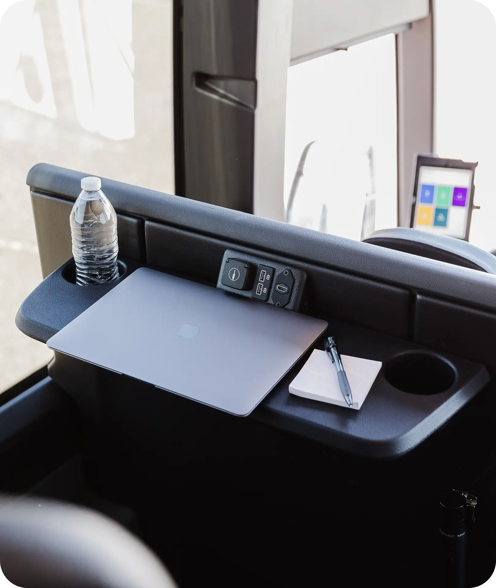 A laptop and notepad on a fold-down tray with USB ports inside an All Aboard America corporate commuter bus