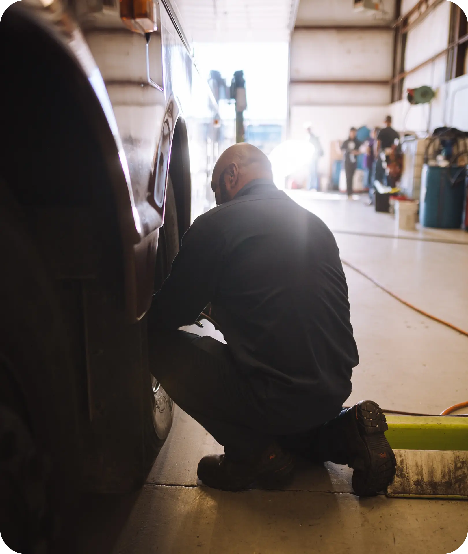 An All Aboard America mechanic crouches beside a bus wheel performing maintenance in the repair shop